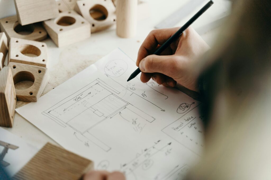 Close-up of a person sketching a wooden toy design in a workshop setting, showcasing creativity and craftsmanship.